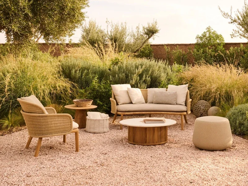 Khu sân vườn ngoài trời với sofa trắng, ghế mây và bàn tròn giữa thảm sỏi